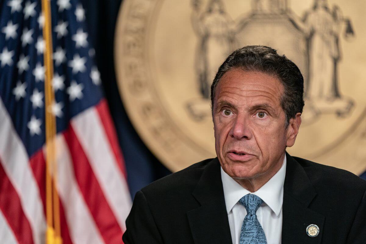 Andrew Cuomo Gubernur New York mengenakan jas hitam, tampak bendera Amerika Serikat